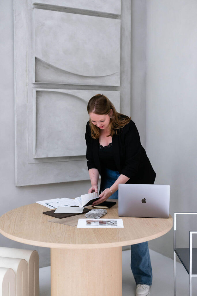 Interieurontwerper staand over tafel met materialen, tekeningen en laptop voor masterplan traject